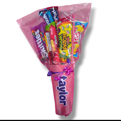 Candy bouquet wrapped in pink cellophane and ribbon with assorted candy and a personalized cup