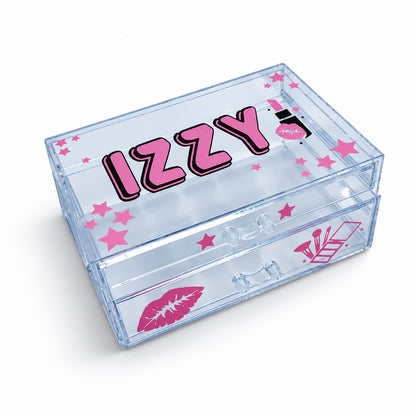 A clear acrylic cosmetic organizer box with pink lettering that reads 'IZZY' and pink lip print graphics, shown on a light gray surface.